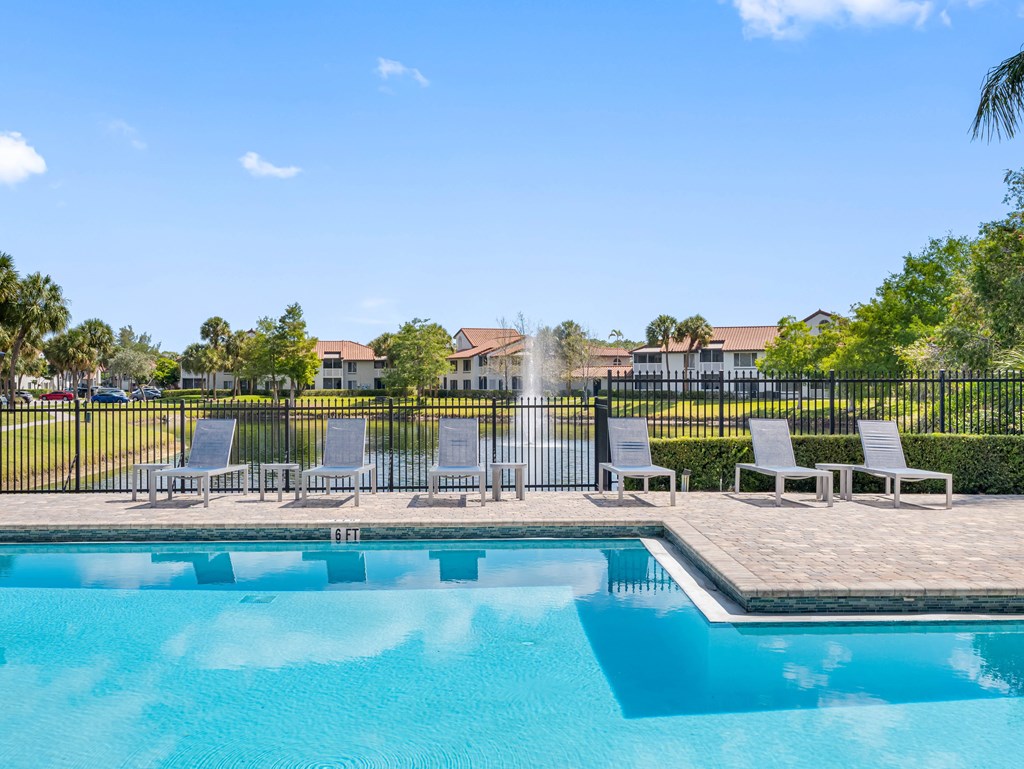 A pool with a fence and chairs in front of a building.